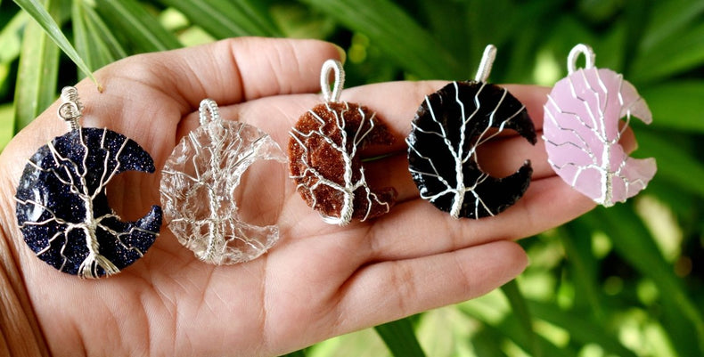 Hand holding five moon-shaped jewelry pieces against a natural background