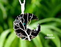 Black obsidian pendant on a white cord against a green blurred background