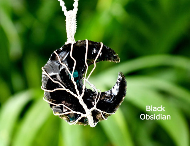 Black obsidian pendant on a white cord against a green blurred background
