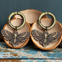 Pair of antique-brass-tone death head moth boot charms with skull motifs and round clip rings