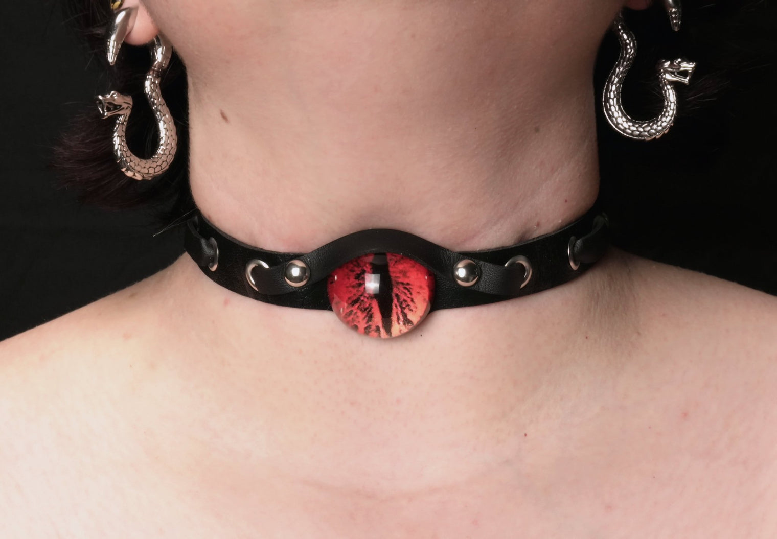 A close-up image of a person wearing a black leather choker collar with a red demon eye at its center.