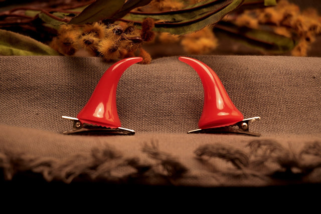 A pair of red devil horns hair clips placed on a textured surface with a neutral background.