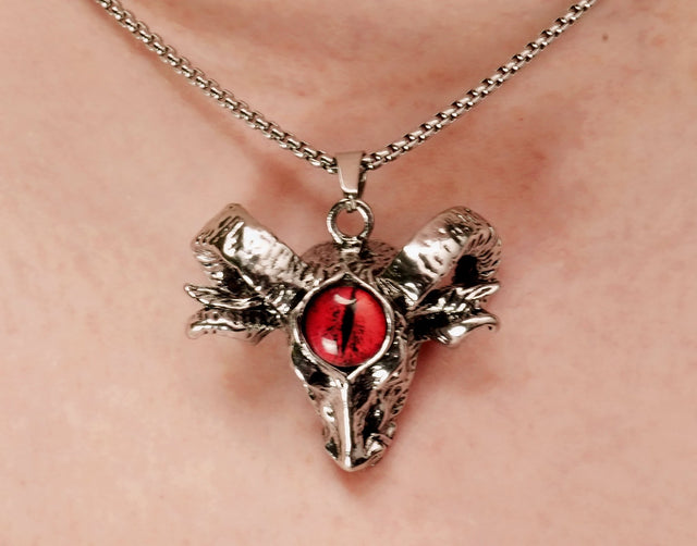 A ram head necklace with a redDevil's eye pendant, suspended from a chain.
