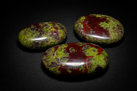 Three polished Dragon Blood Jasper palm stones with deep red and mossy green patterning on black