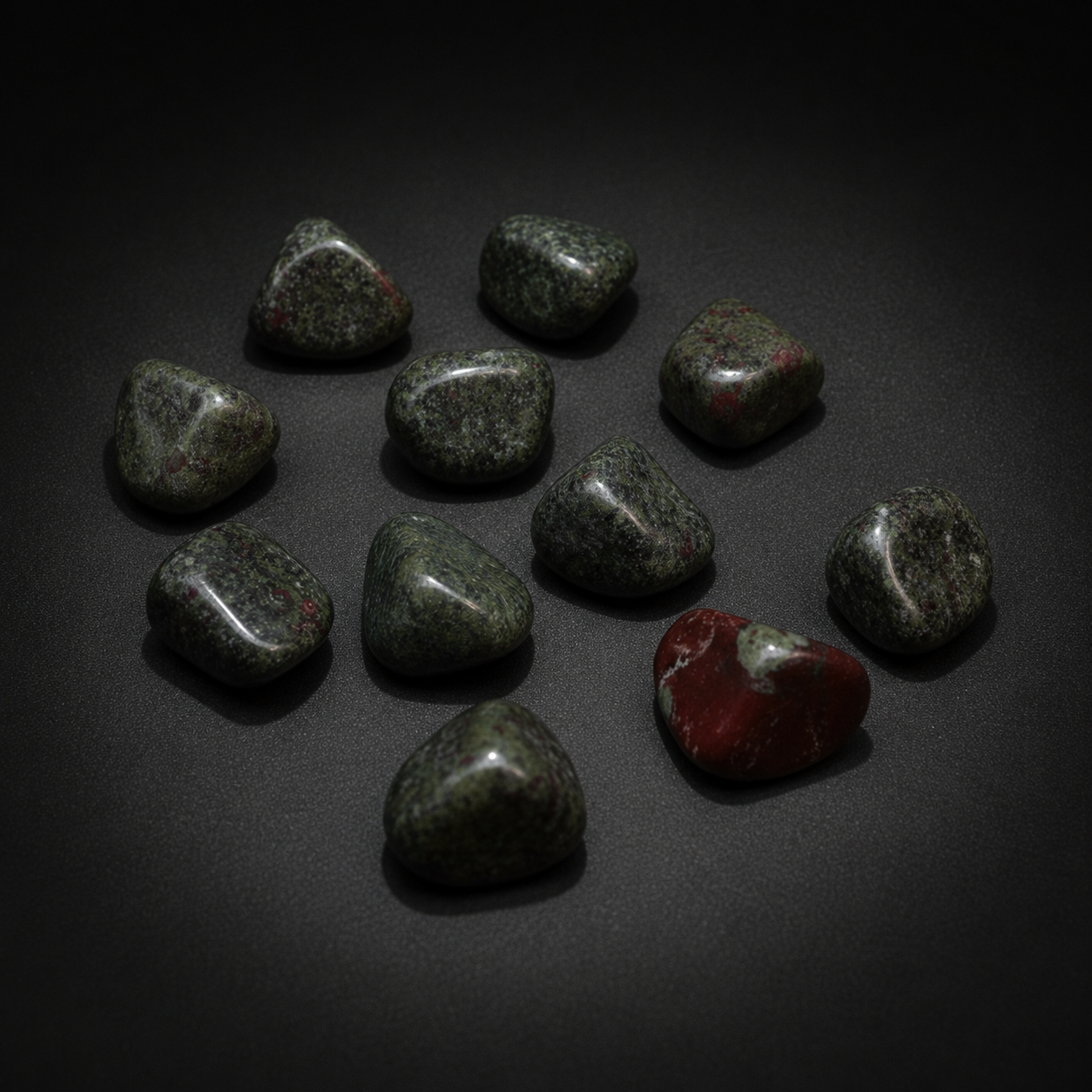 Ten polished green Dragon Bloodstone tumbled stones with naturally varied red markings on a matte black surface