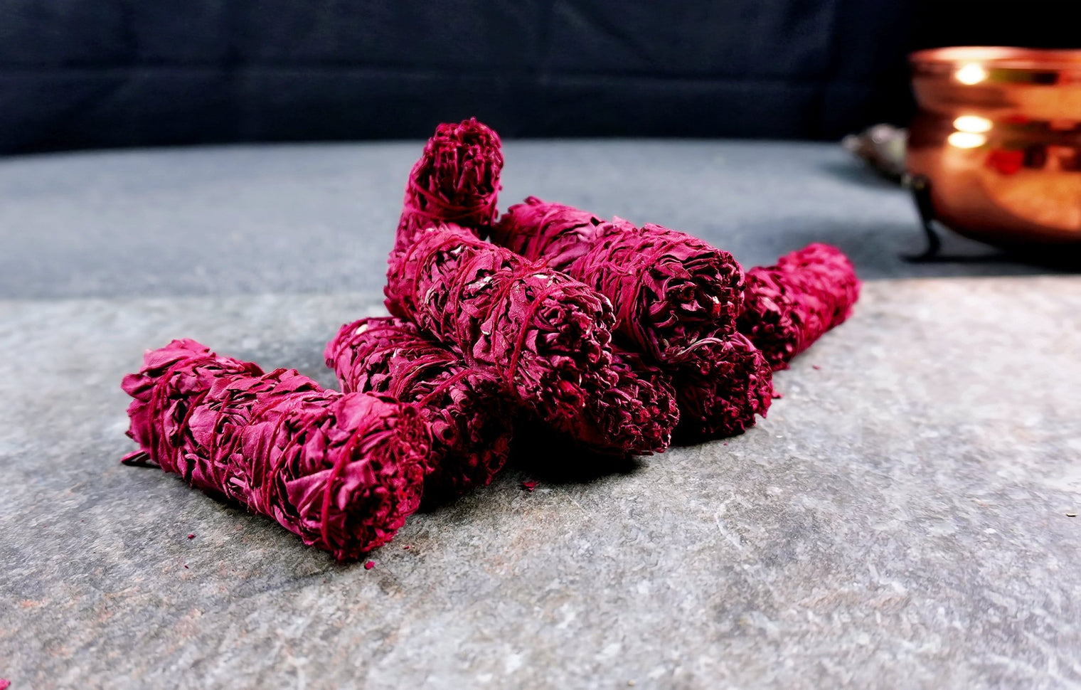 A bundle of red Dragon's Blood Smudge Sticks laid on a gray surface, with a copper object in the background.