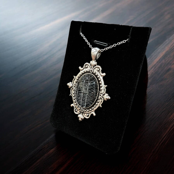 Small silver-tone filigree cabochon necklace containing real spiderweb