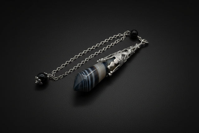 Silver pendulum with blue stones on a white surface with crystal rock and greenery