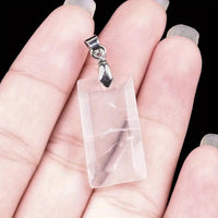 Clear quartz crystal pendant with silver hook held in hand against a black background
