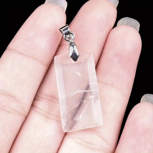 Clear quartz crystal pendant with silver hook held in hand against a black background
