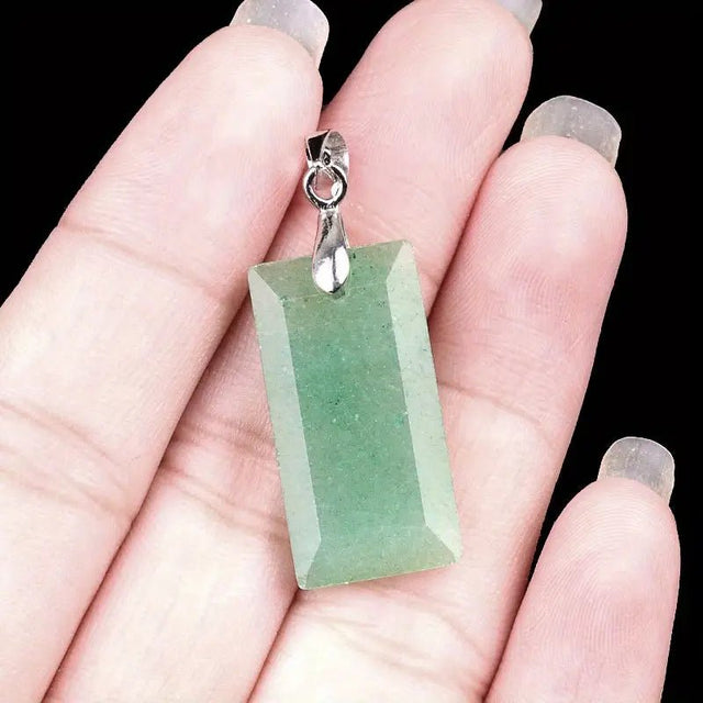 Green aventurine rectangular pendant on a hand with a black background