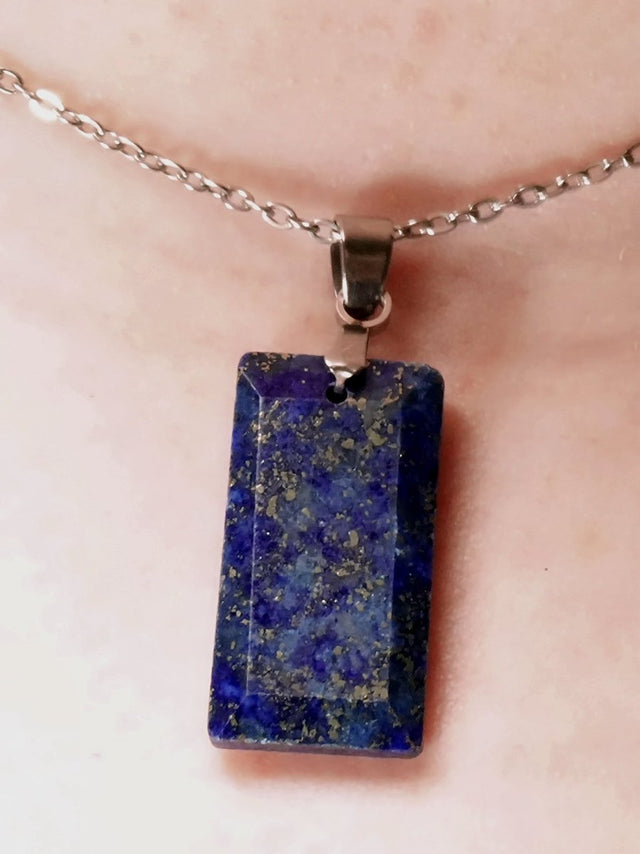 A faceted lapis lazuli pendant necklace with pyrite inclusions, suspended from a silver chain on a person's neck.