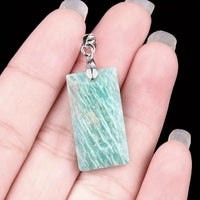 Hand holding a pendant with a green amazonite marbled stone and silver clasp against a black background