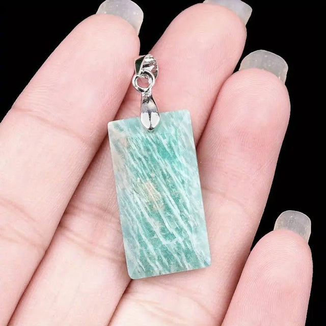 Hand holding a pendant with a green amazonite marbled stone and silver clasp against a black background
