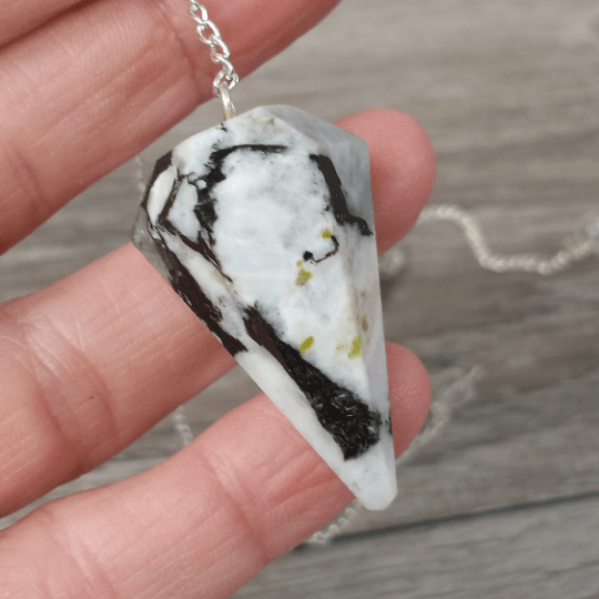 Necklace with a unique stone pendant held by a hand on a wooden surface