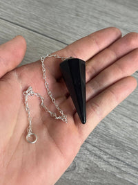 Black pyramid-shaped pendant on a silver chain held in a hand against a wooden background