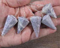 Five stone pendants on silver chains held in a hand with a wooden surface background.