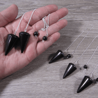 Black cone-shaped pendants on silver chains held in a hand, with additional pendants on a wooden surface.