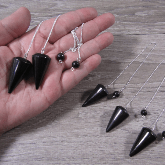 Black cone-shaped pendants on silver chains held in a hand, with additional pendants on a wooden surface.