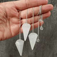 Hand holding three crystal pendulums on chains against a neutral background