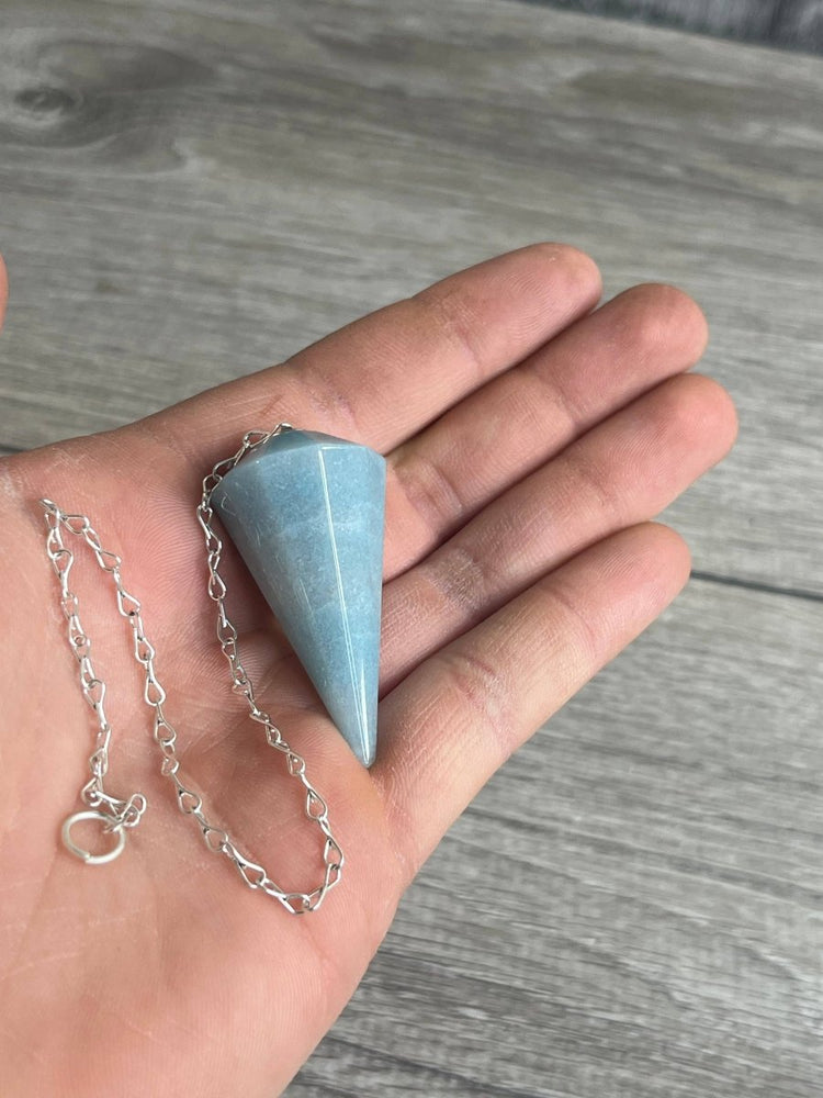 Hand holding a silver necklace with a blue stone pendant on a wooden surface
