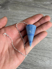 Blue stone pendant on a silver chain held in a hand against a wooden background