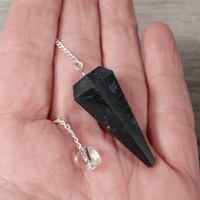 Black crystal pendant on a chain held in a hand