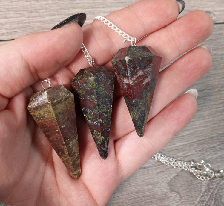 Three stone pendants on a silver chain held in a hand against a wooden background