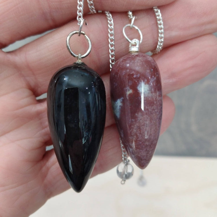 Two black and purple stone pendants on silver chains held in a hand.