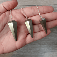 Three geometric pendant necklaces on a hand with a wooden background