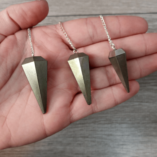 Three geometric pendant necklaces on a hand with a wooden background
