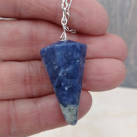 Blue stone pendant on a chain held in a hand with a blurred background