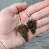 Two stone pendulums on a chain held in a hand against a wooden surface.
