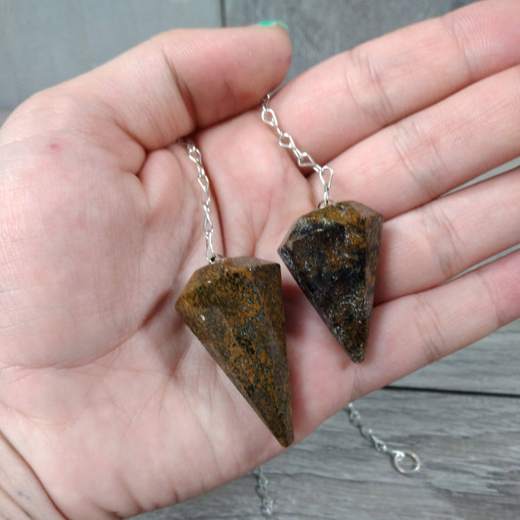 Two stone pendulums on a chain held in a hand against a wooden surface.