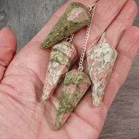 Hand holding four green and pink stone pendulums on a wooden surface