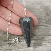 Black crystal pendant on a silver chain held by a hand on a wooden surface