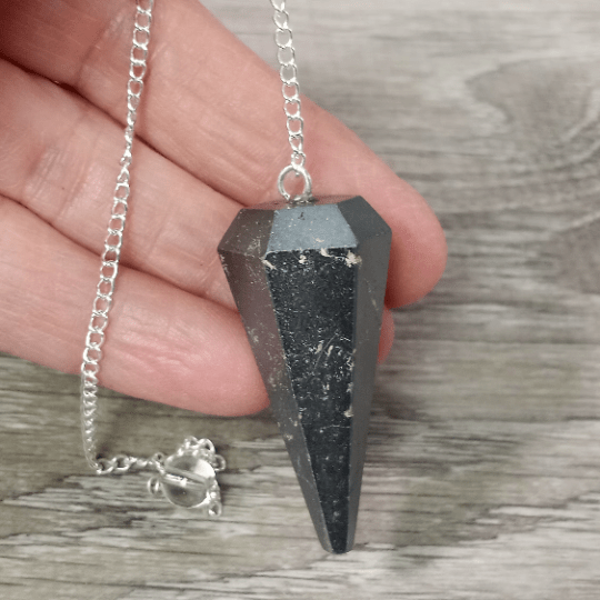 Black crystal pendant on a silver chain held by a hand on a wooden surface