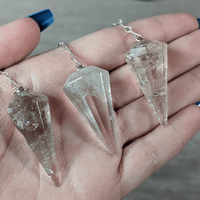 Three crystal pendants on silver chains held in a hand.