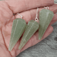 Three green crystal pendants on silver chains held in a hand against a wooden surface.