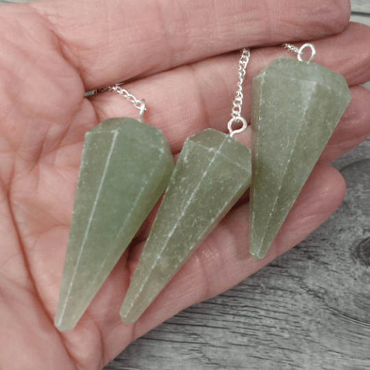Three green crystal pendants on silver chains held in a hand against a wooden surface.