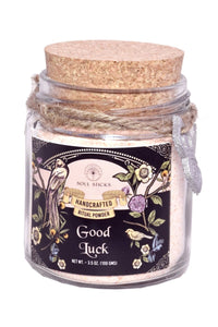 Jar of 'Good Luck' ritual powder with decorative label and cork lid on a white background