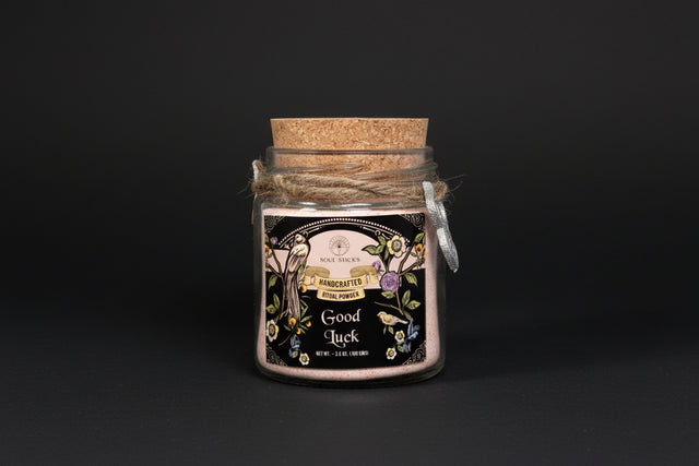Jar of 'Good Luck' ritual powder with decorative label and cork lid on a white background
