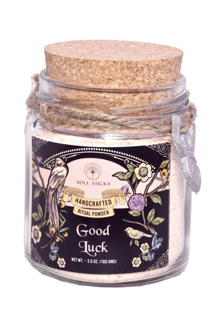 Jar of 'Good Luck' ritual powder with decorative label and cork lid on a white background