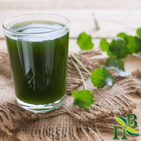 Glass of green juice with fresh green leaves on a woven mat, featuring a brand logo in the corner.