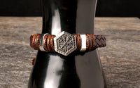 A hand-woven leather bracelet with a silver Vegvisir charm displayed on a dark bottle.