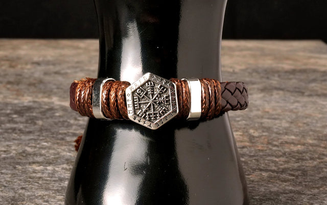 A hand-woven leather bracelet with a silver Vegvisir charm displayed on a dark bottle.