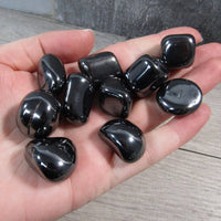 Hand holding a collection of glossy black stones on a wooden surface