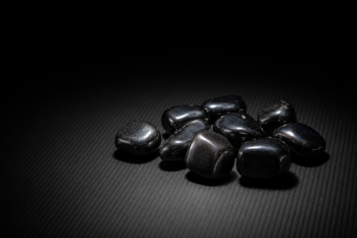 Small group of polished gunmetal-gray Hematite tumbled stones on a ribbed matte black surface