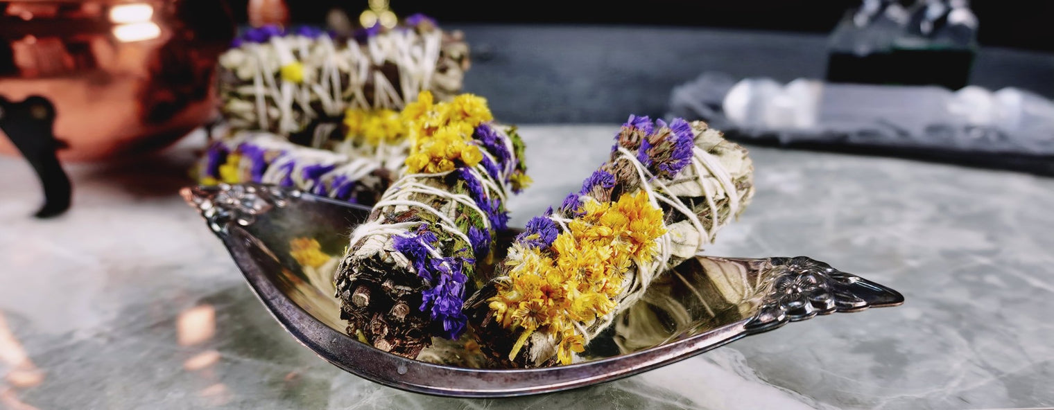 A smudge stick with a blend of Mullein, Statice, and Yerba Santa herbs, bound together and presented on a dish, with a background suggesting a relaxed, magical atmosphere.