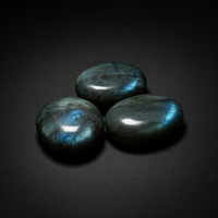 Three polished dark gray labradorite palm stones showing blue-green flash on a matte black surface